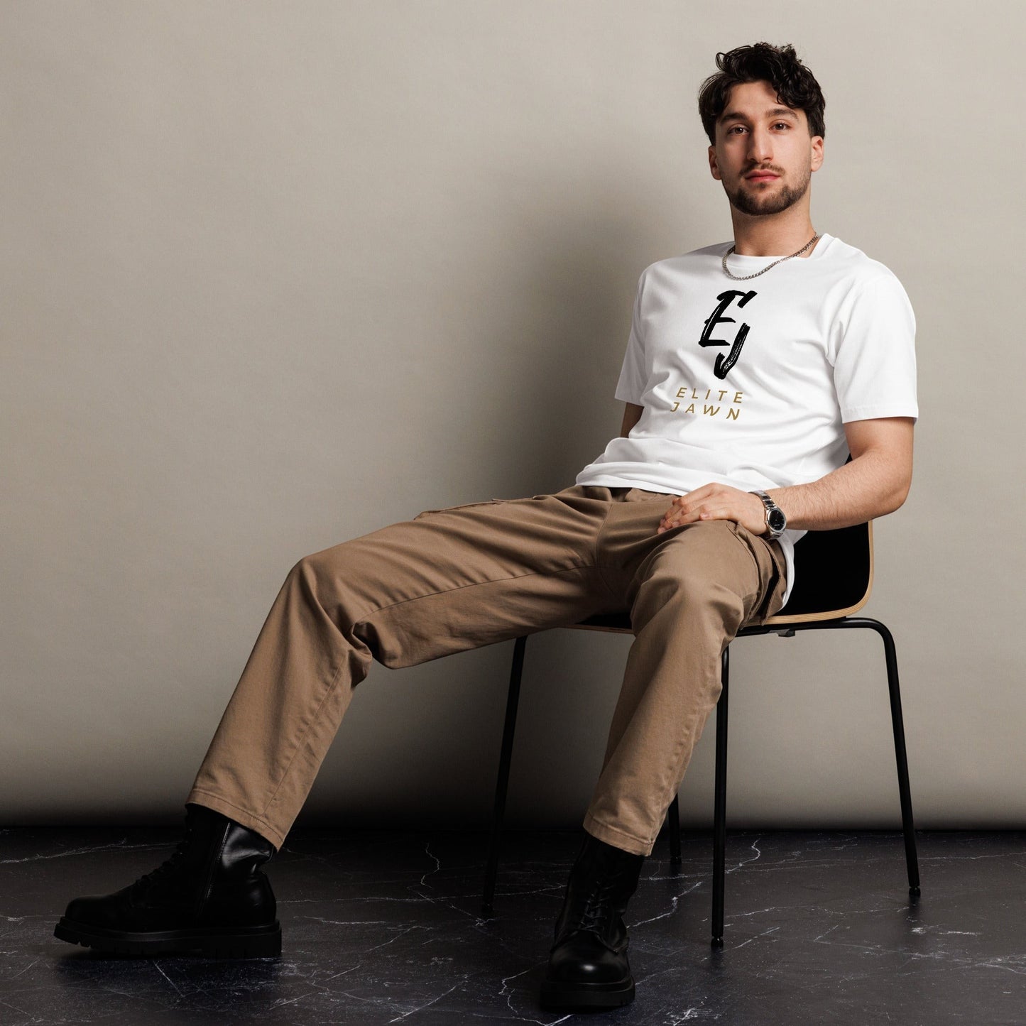 Elite Jawn white 100% combed cotton crewneck t-shirt with black and gold logo on chest. Model seated.